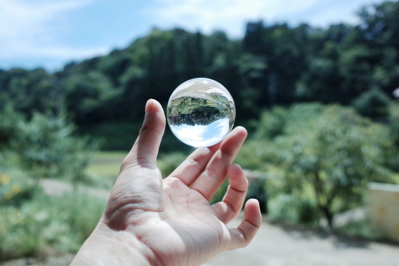 Transparenz Eine Hand hält eine Kristallkugel, die die Landschaft im Hintergrund reflektiert.